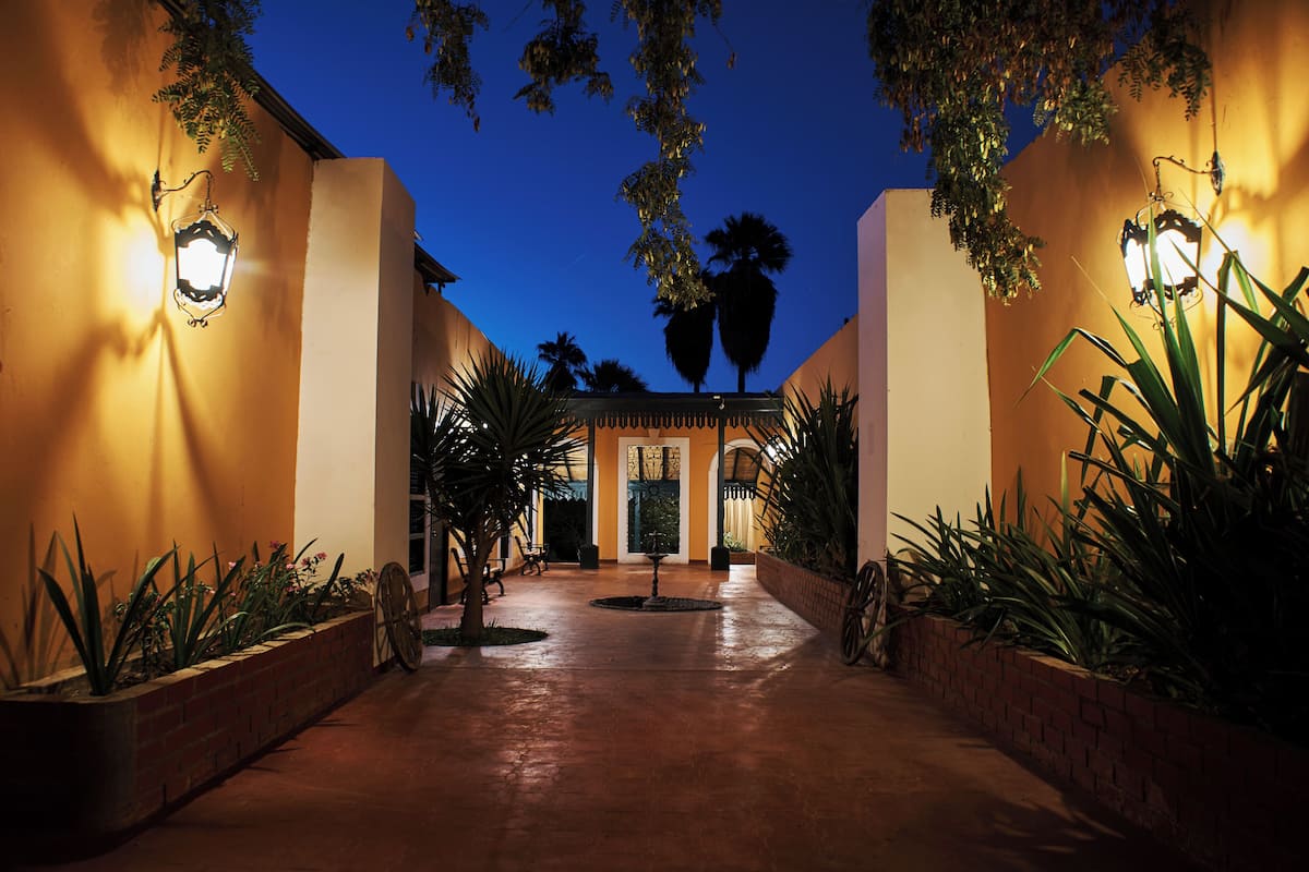 A well-lit entrance with a brick pathway, palm trees, and a building facade with a door and windows.