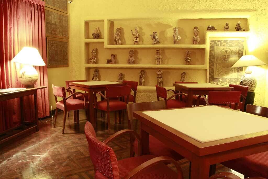 A room with wooden tables and red chairs, a red curtain, and shelves with small figurines.
