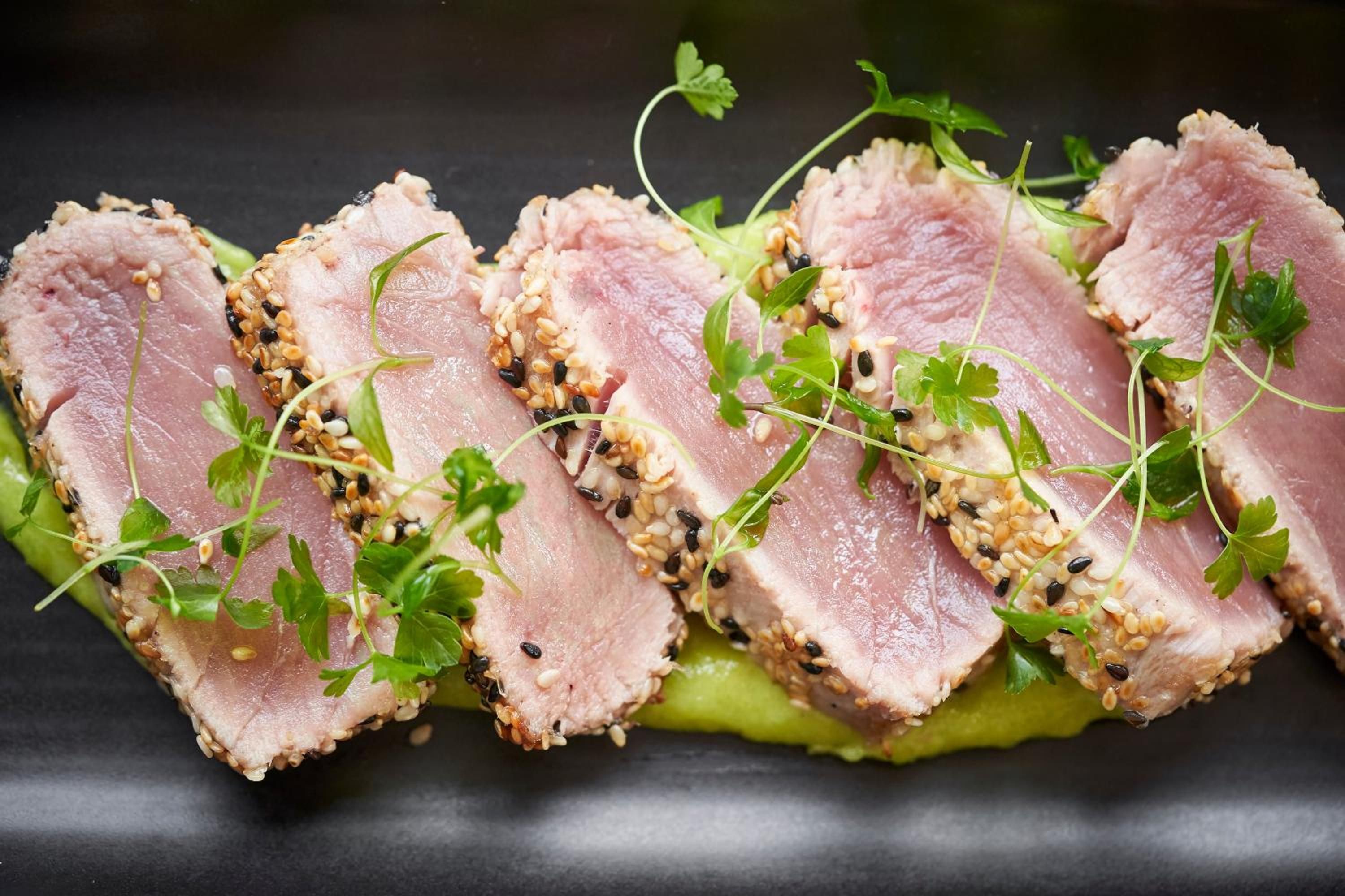 A close-up of sliced meat garnished with sesame seeds and herbs.
