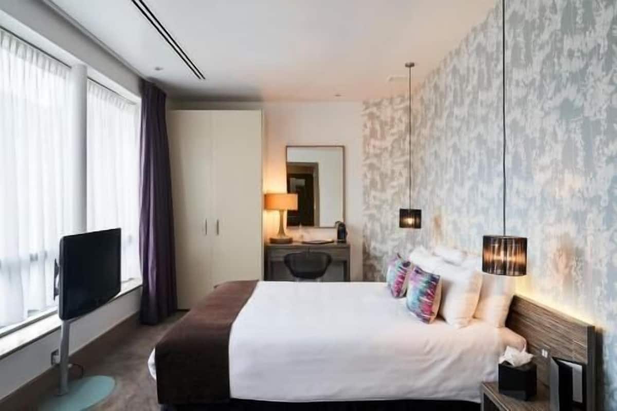 Quarto de hotel com cama, mesa de cabeceira, luminária e vista para o exterior.