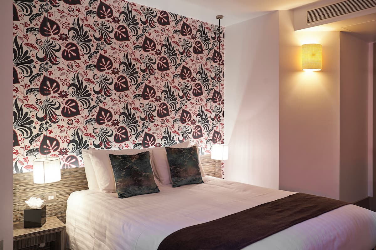 Quarto de hotel com uma cama grande, duas luminárias de cabeceira, uma parede com padrão floral e um respiradouro no teto.