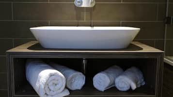 A bathroom with a white vessel sink, a towel rack, and a towel storage area.