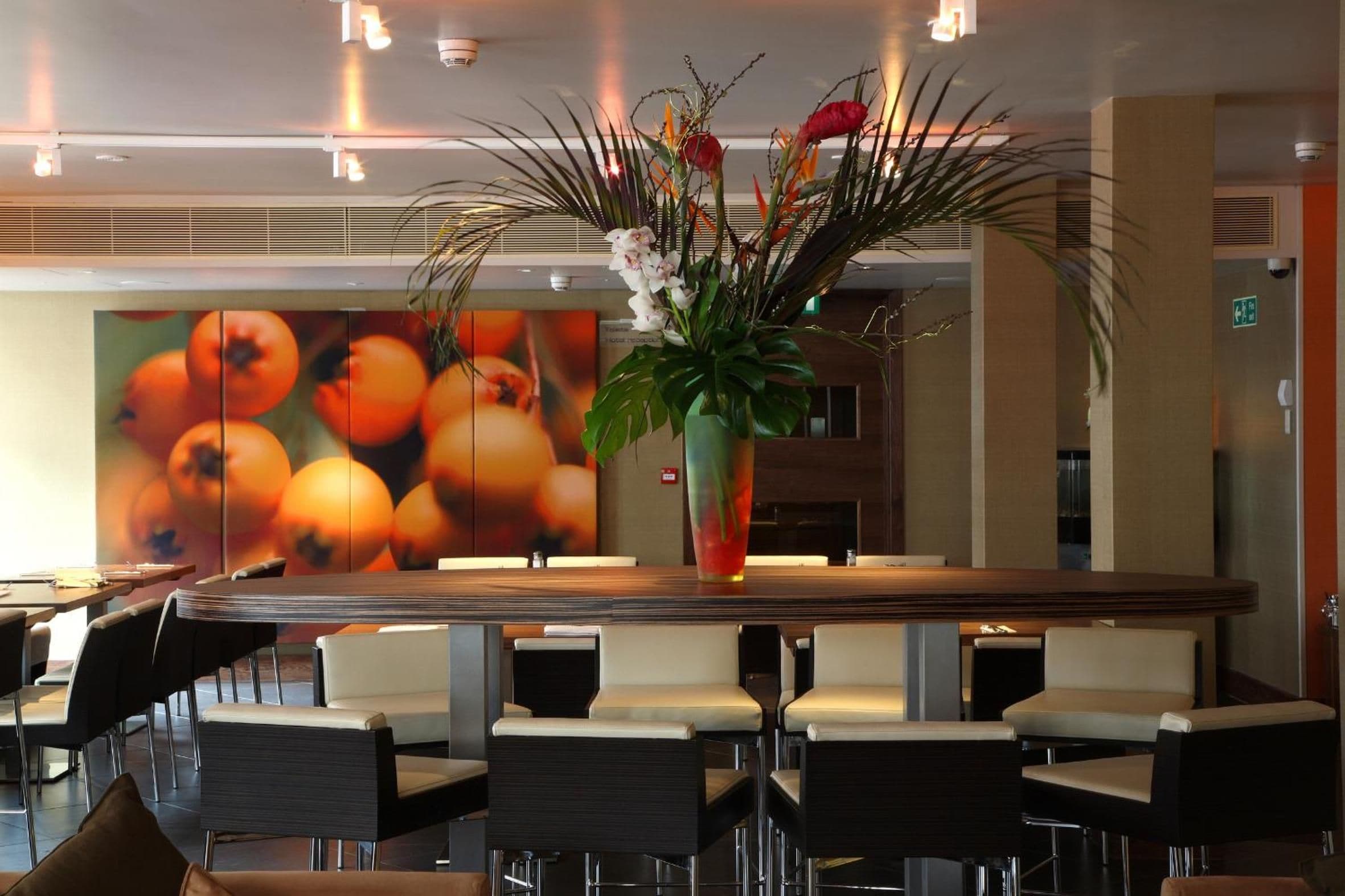 Una moderna hall d'hotel con scrivania della reception, zona salotto e una parete decorata con una composizione di frutta arancione.