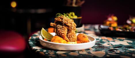 A plate of fried chicken with lime wedges and a side of greens on a table with a mosaic pattern.