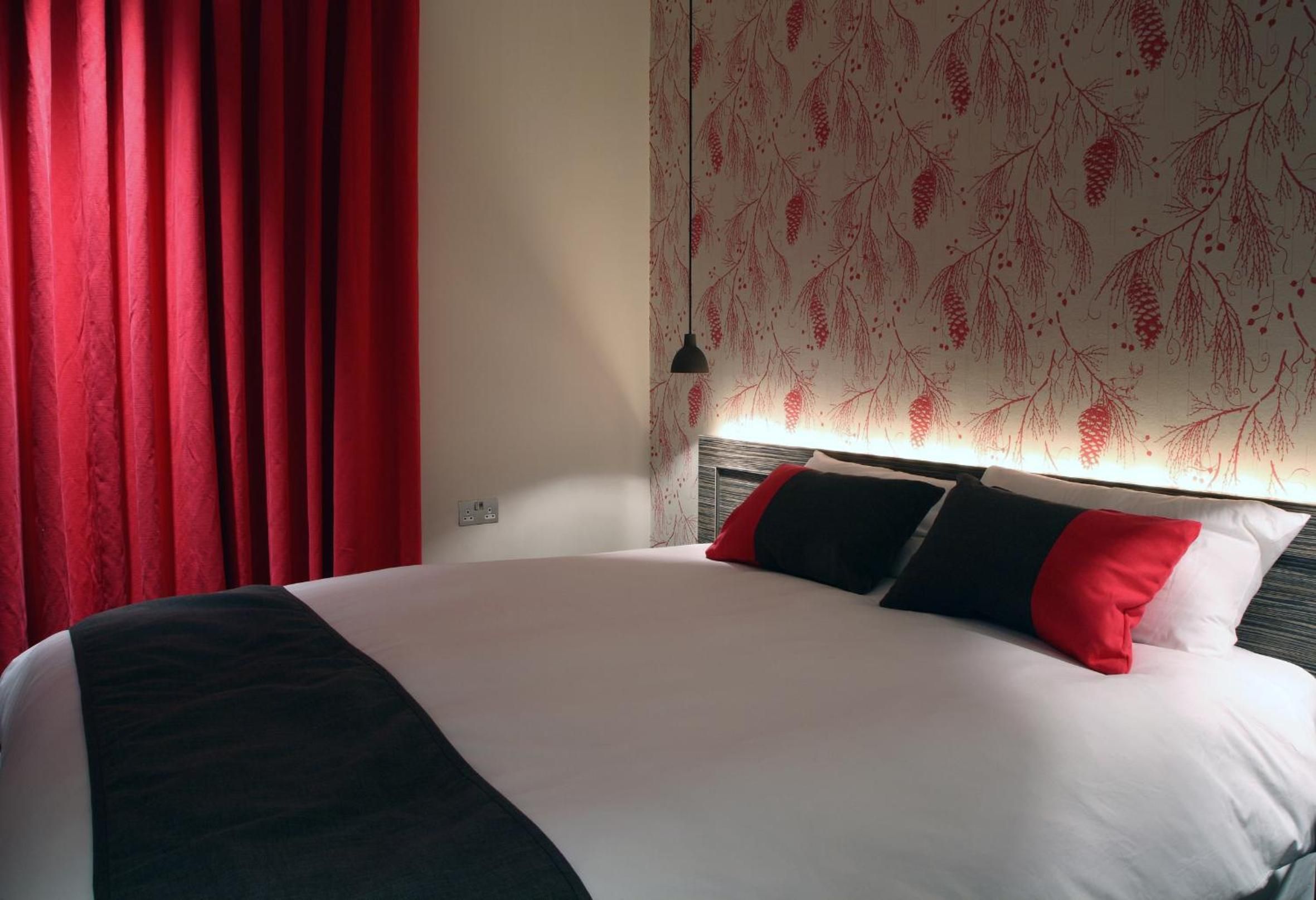 Una habitación de hotel con una cama, cortinas rojas y un panel decorado con un diseño de ramas de pino.