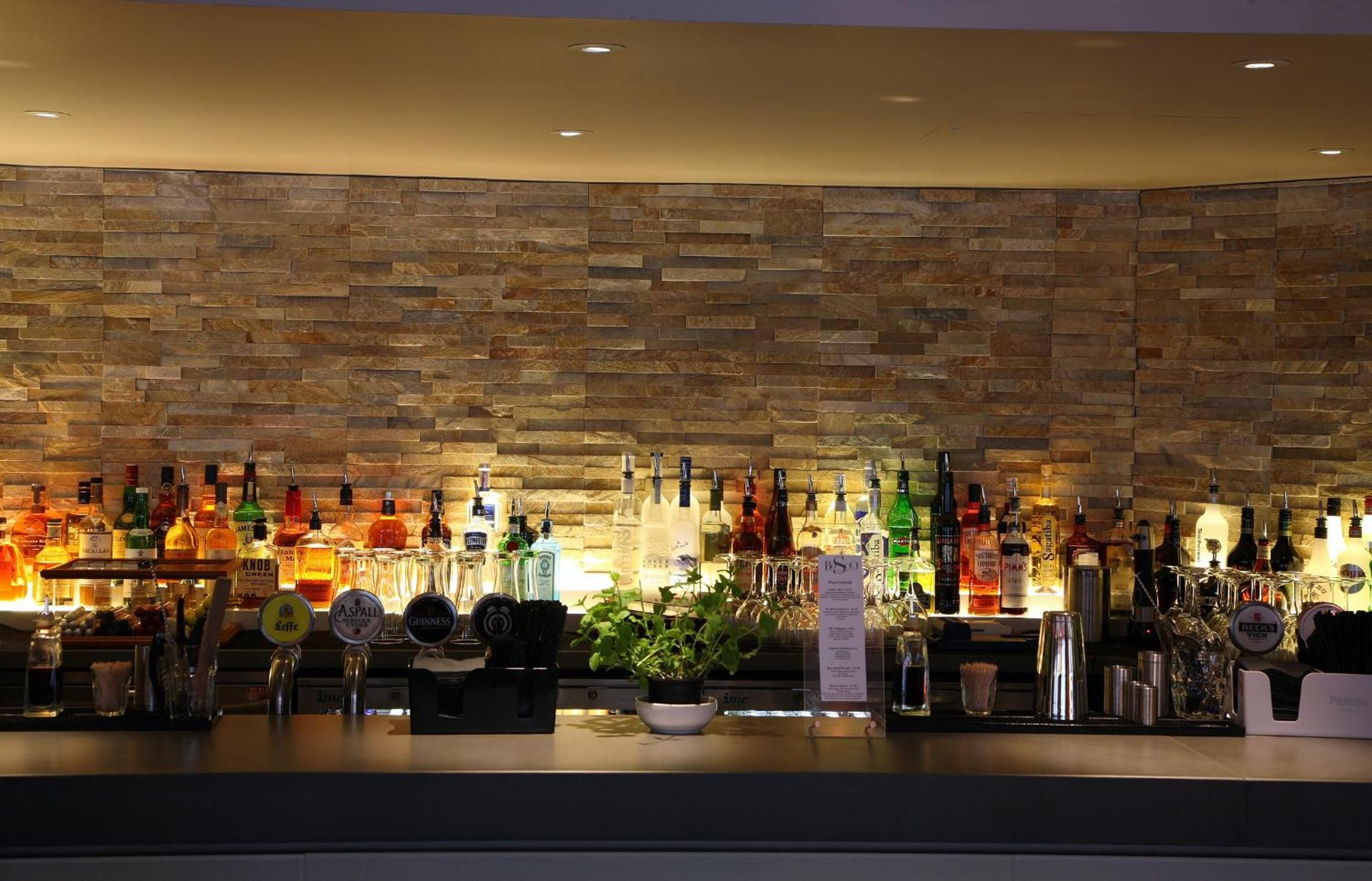 A bar area with a stone wall backdrop and a variety of liquor bottles.