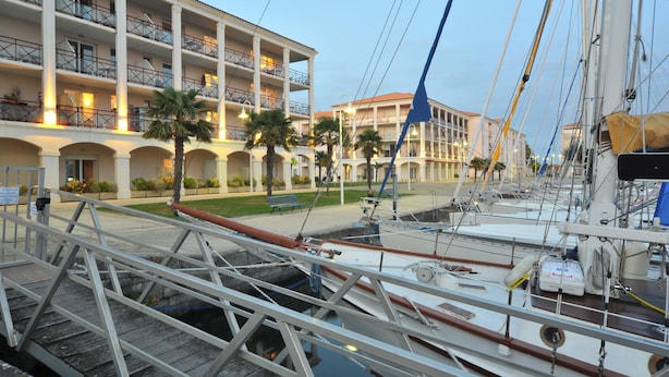Una marina con barcos amarrados, un edificio con balcones y un paseo para peatones.