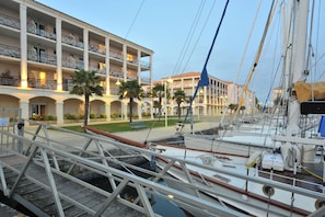 A marina with boats docked, a building with balconies, and a pedestrian walkway. - Residences de Bougainville (Rochefort)
