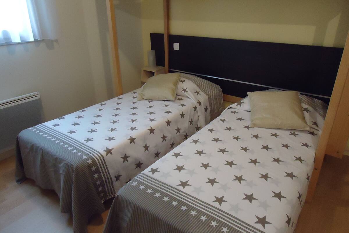 Quarto com duas camas de solteiro, cada uma com colcha e almofadas estampadas com padrão de estrelas.
