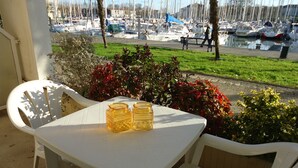 Un patio con una mesa y sillas blancas, dos frascos de vidrio y vistas a un puerto deportivo con barcos.