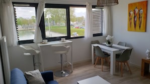 Una sala de estar moderna con un sofá, una mesa de comedor con sillas y vistas a un parque a través de amplios ventanales.