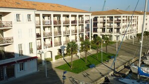 Un hotel de varios pisos con balcones, un estacionamiento y un puerto deportivo con barcos.
