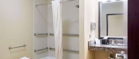 A bathroom with a bathtub, a shower, a vanity with a mirror, a towel rack, and a hand dryer.