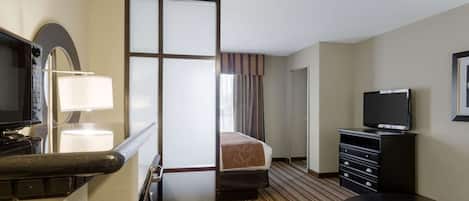 A hotel room with a bed, a TV, a desk with a lamp, a chair, and a sliding door.