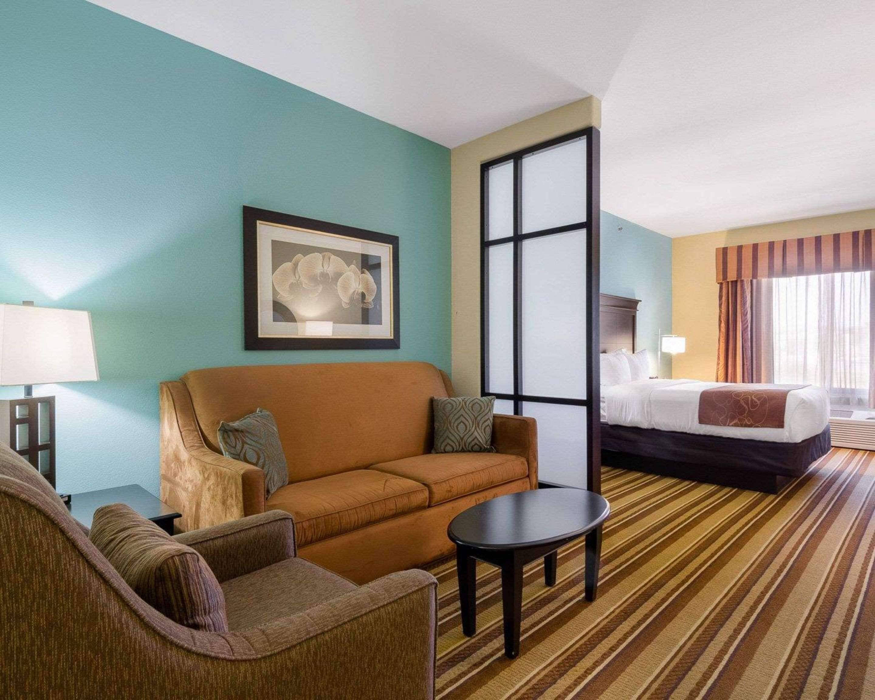 A hotel room with a sofa, armchair, and a bed with a striped curtain.