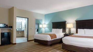 A hotel room with two beds, a desk, a mirror, and a bathroom visible through an open door.