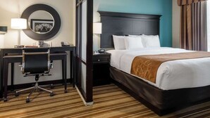 A hotel room with a bed, desk, chair, and a large mirror.