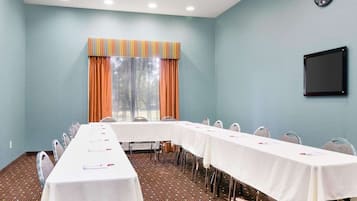 A conference room with a long table, chairs, a clock, and a window with curtains.
