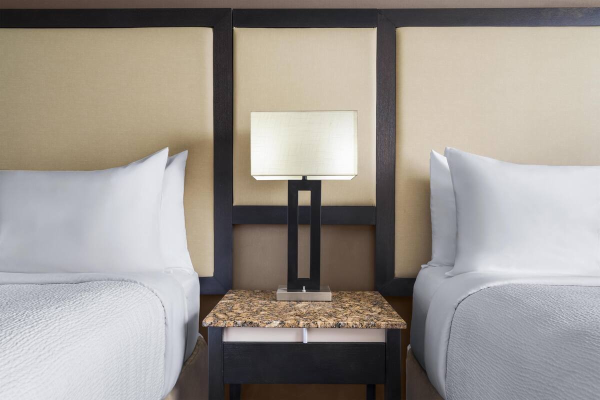 A hotel room with two beds, a small bedside table, and a lamp.