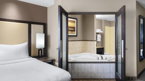 A hotel room with a large bed, a bathroom with a bathtub, and a mirror. - Best Western Premier Freeport Inn Calgary Airport (Calgary)