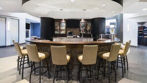 A modern bar area with a curved counter, four bar stools, and a television above the bar. - Best Western Premier Freeport Inn Calgary Airport (Calgary)