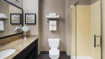 A modern bathroom with a granite countertop, a toilet, a glass shower enclosure, and framed artwork on the wall.