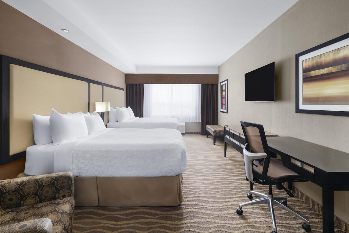 A hotel room with two beds, a desk, a chair, a television, and a large window.