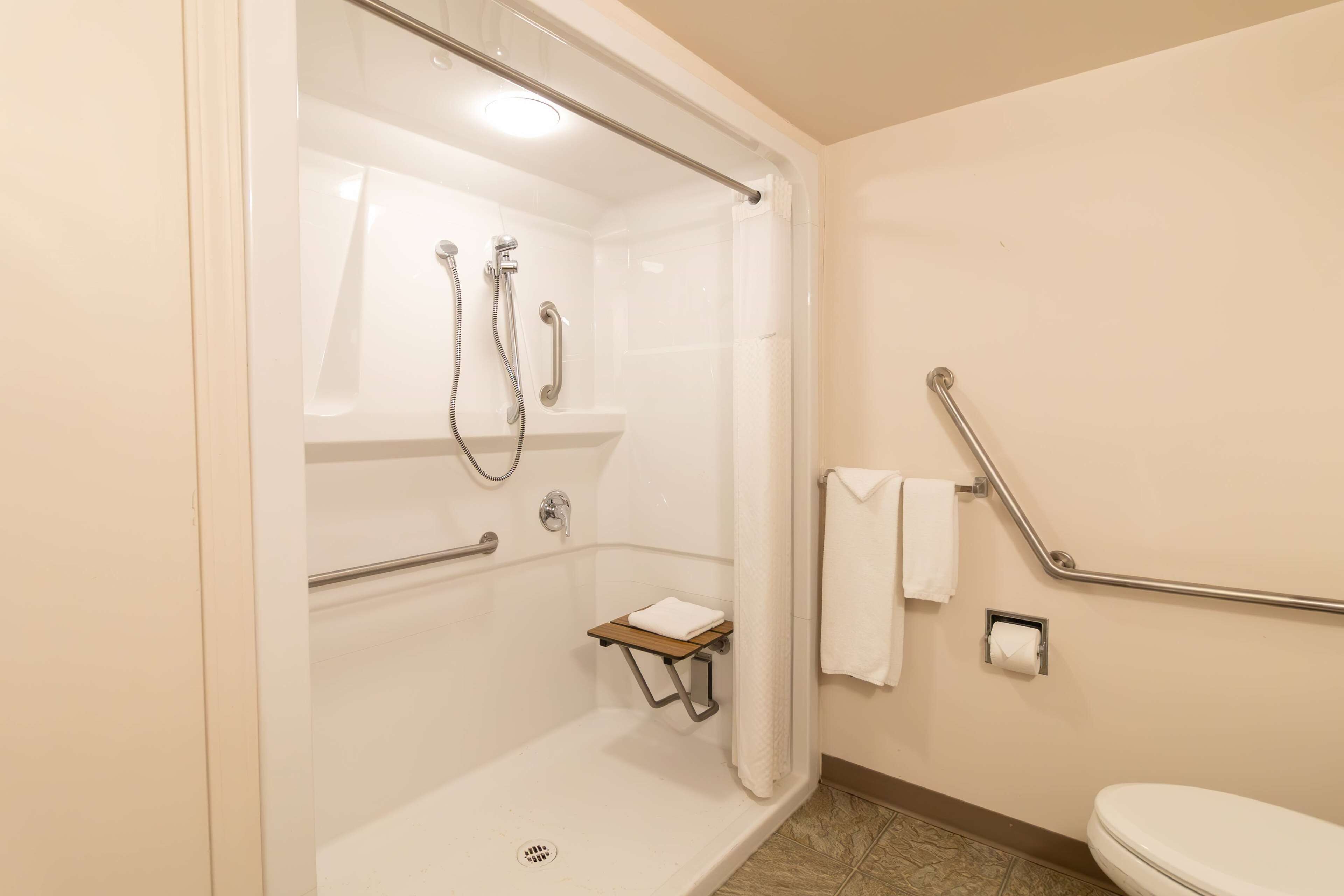 A shower with a glass door, a grab bar, a towel rack, and a toilet with a grab bar.