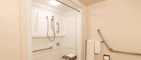 A shower with a glass door, a grab bar, a towel rack, and a toilet with a grab bar.