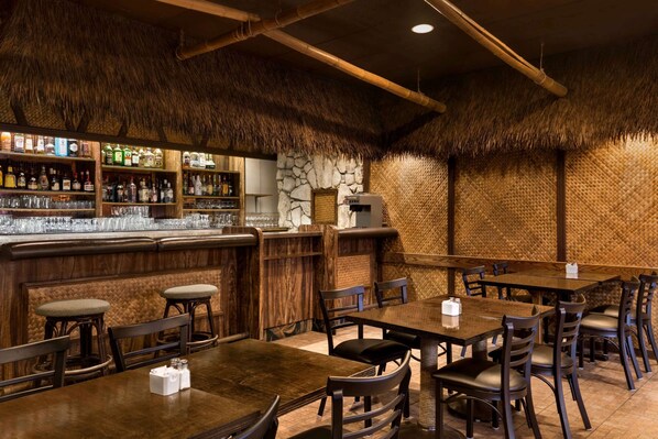 A restaurant with wooden tables and chairs, a bar area with shelves of bottles, and a stone wall. - Super 8 by Wyndham Prince George (Prince George)