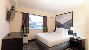 Habitación de hotel con cama, escritorio, televisión, ventana con cortinas, mesita de noche y un cuadro en la pared.