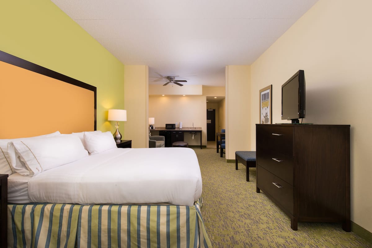 A hotel room with a bed, a desk, a chair, a television, and a ceiling fan.