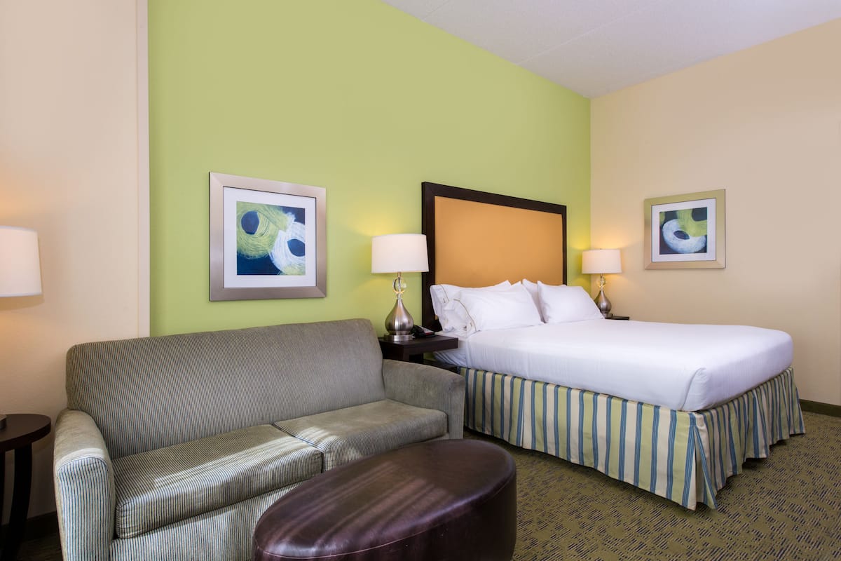 A hotel room with a bed, a sofa, a nightstand, two lamps, and two framed pictures on the walls.