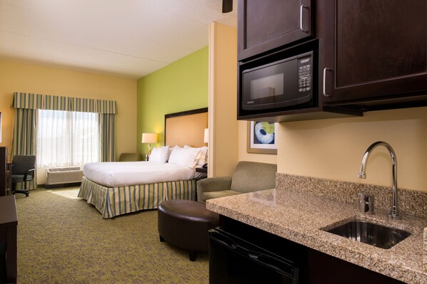 Ein Hotelzimmer mit einem Bett, einem Schreibtisch, einem Stuhl und einer Küchenzeile mit Mikrowelle und Spüle.