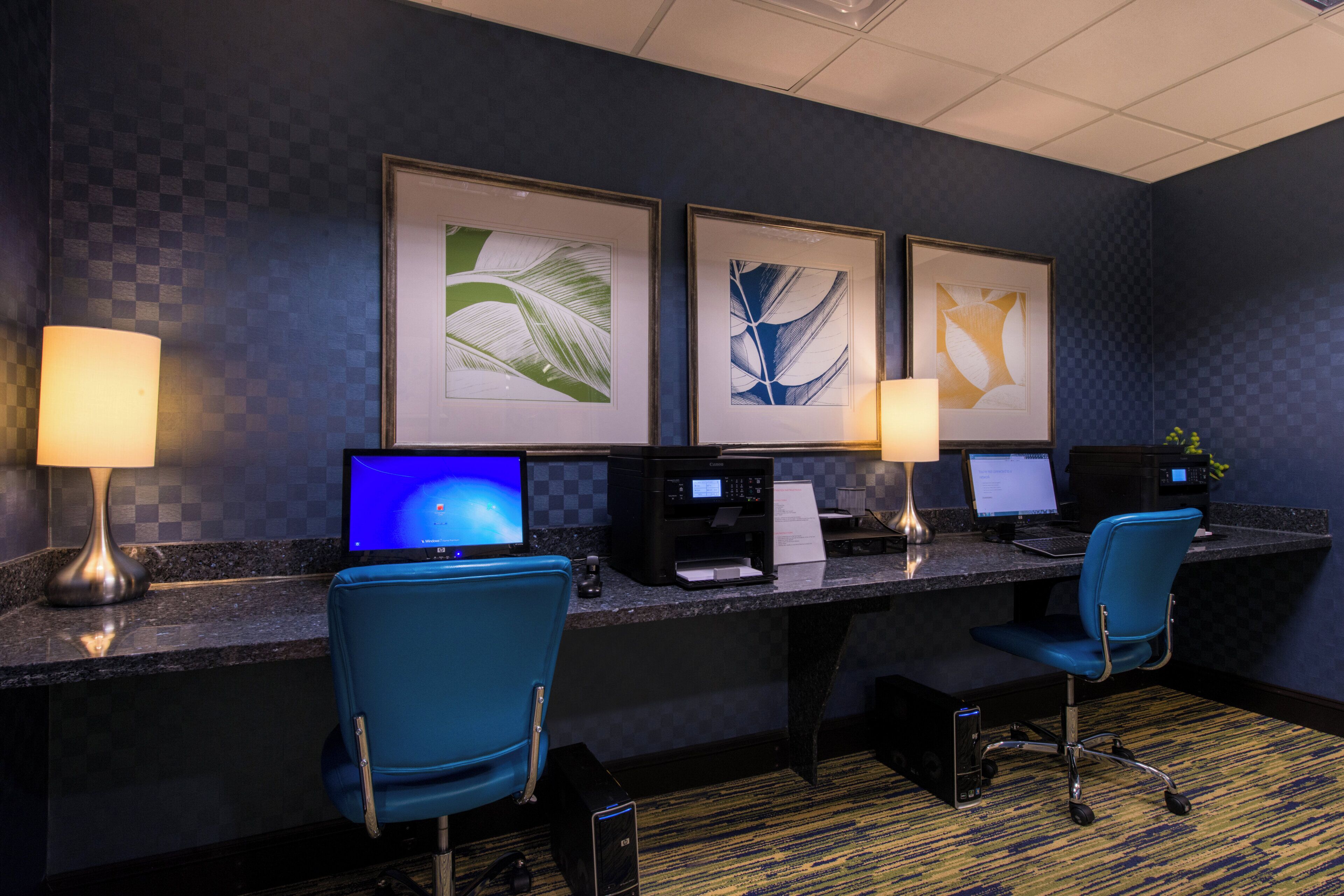 A hotel reception desk with two computer monitors, a printer, and a blue chair.