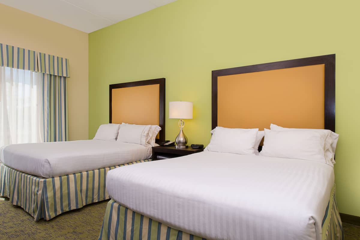 A hotel room with two beds, a nightstand with a lamp, and a window with curtains.