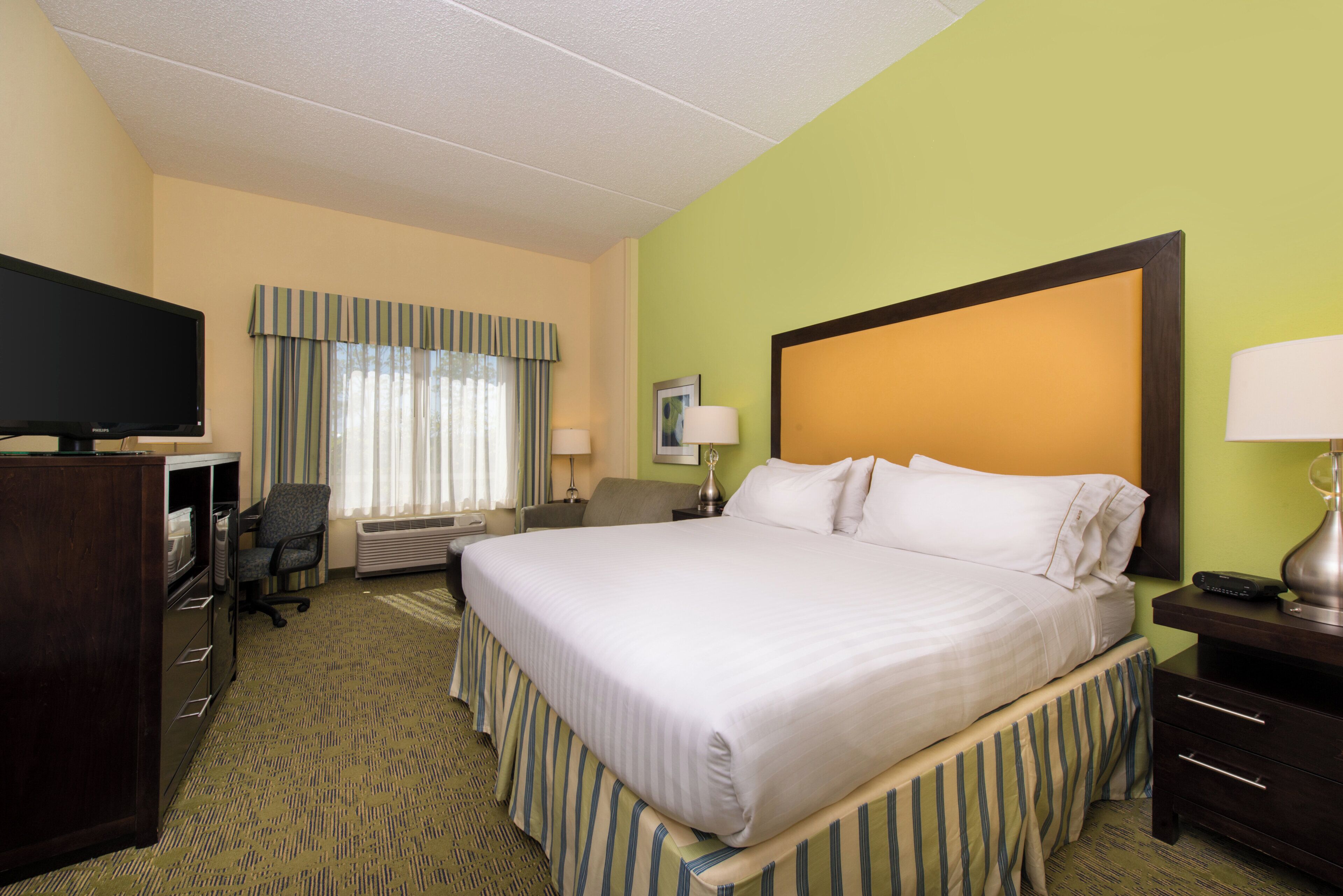 A hotel room with a large bed, a desk with a computer, a television, and a window with curtains.