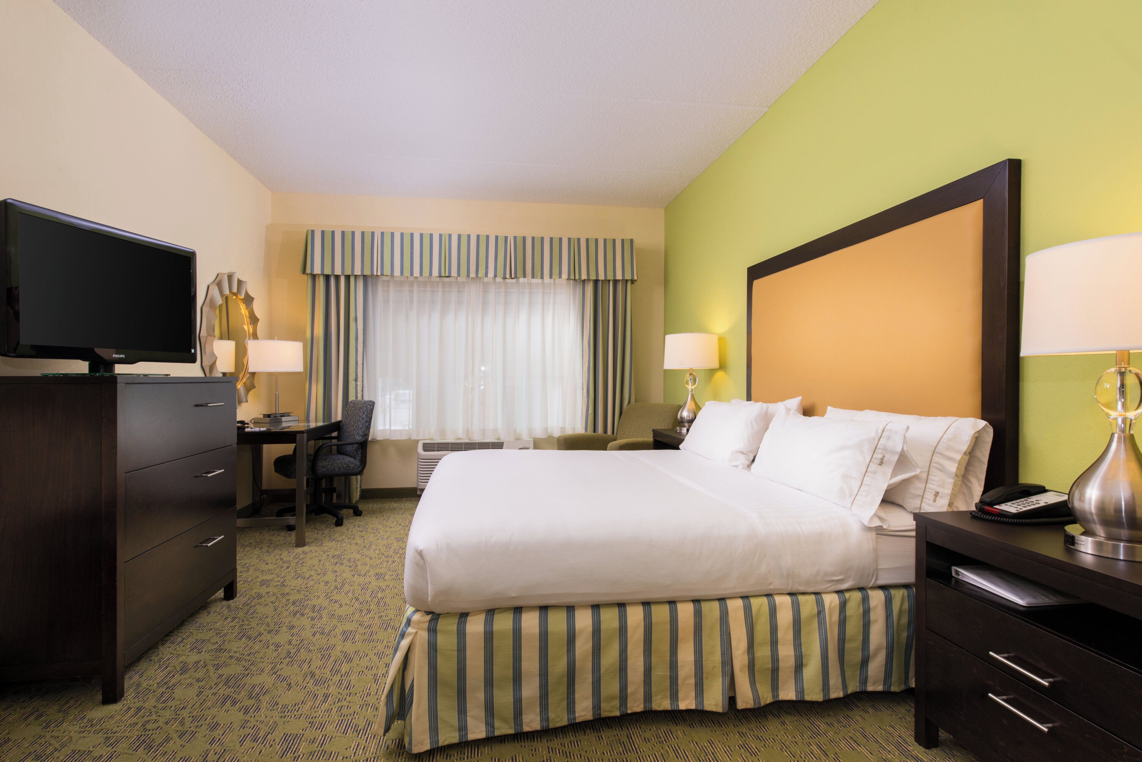 A hotel room with a bed, desk, television, and lamps.
