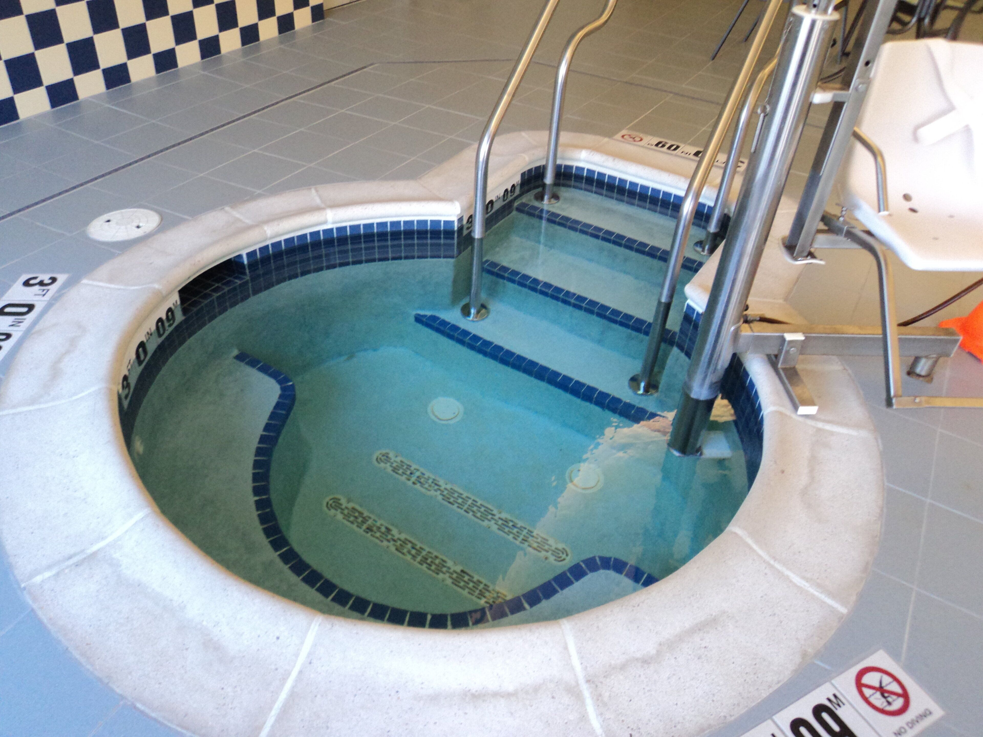 A swimming pool with a checkered floor pattern, a no diving sign, and a pool ladder.