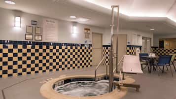 Une salle de bain d’hôtel avec un mur à carreaux, un jacuzzi et un coin salon avec des chaises et une table.