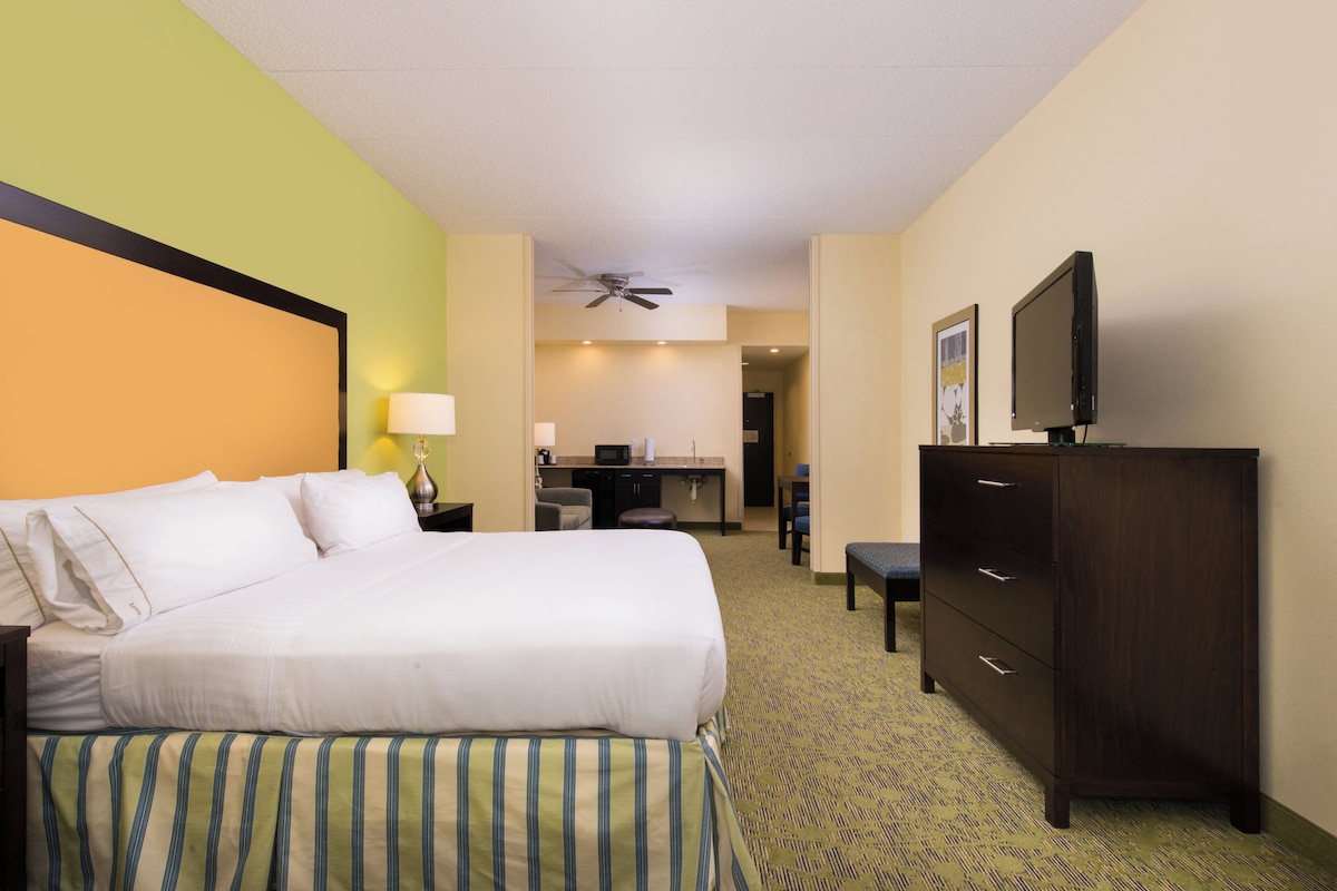 Ein Hotelzimmer mit einem Bett, einem Schreibtisch, einem Sessel, einem Fernseher und einem Deckenventilator.