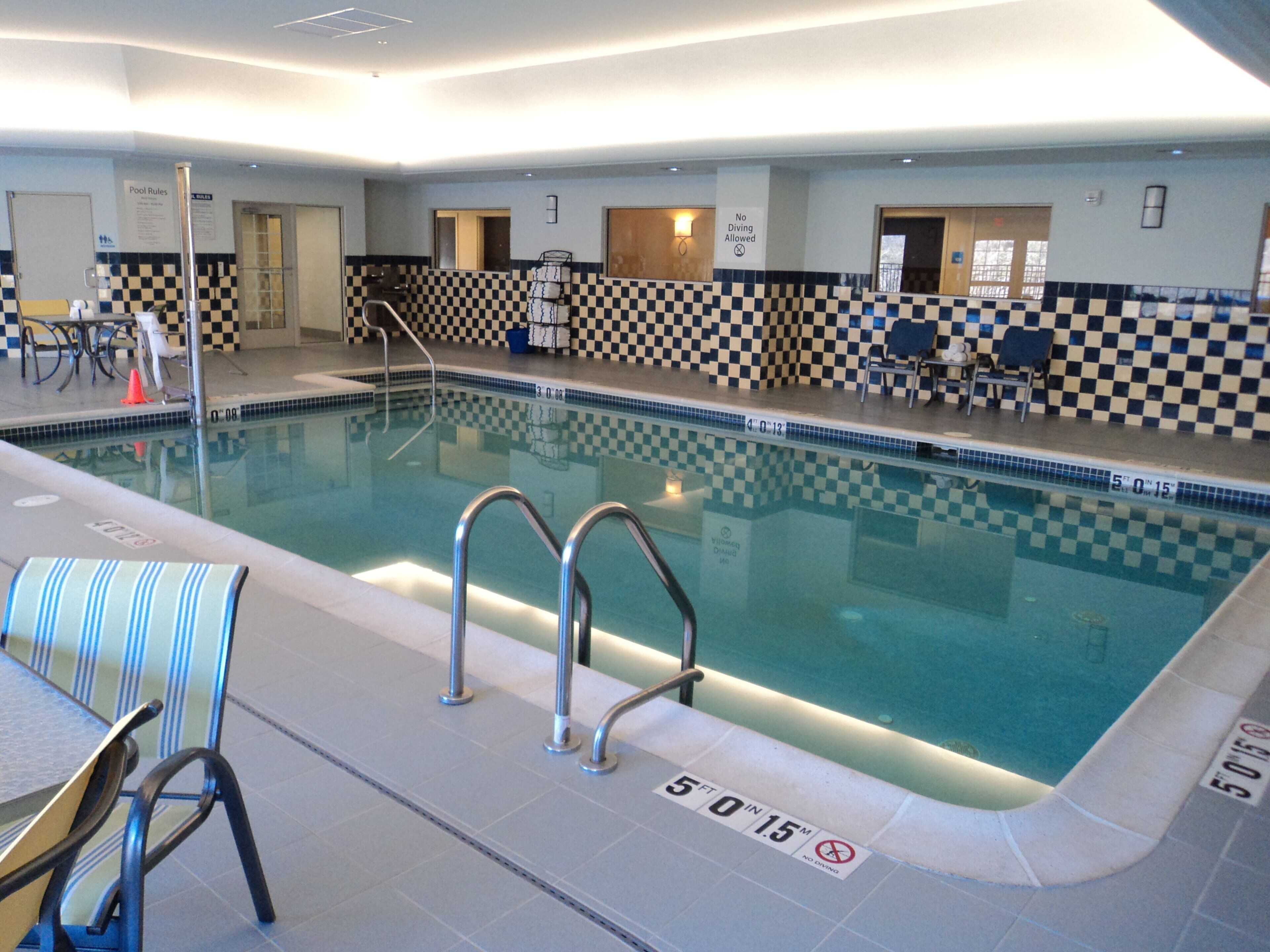 An indoor swimming pool with checkered tiles, a pool ladder, and a sign indicating a depth of 5 feet 0 inches.
