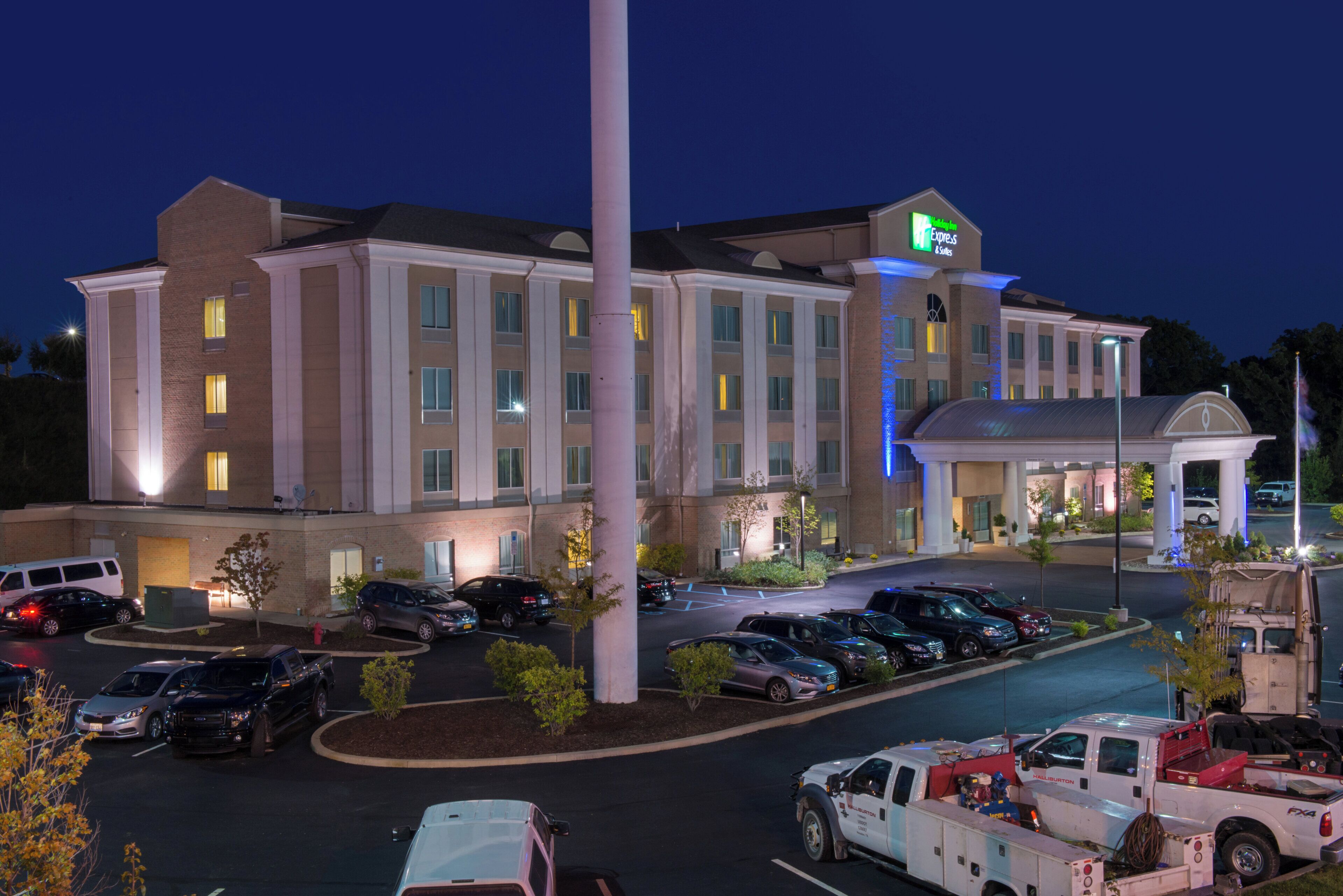 A multi-story hotel with a parking lot, a flagpole, and a large building with illuminated signage.