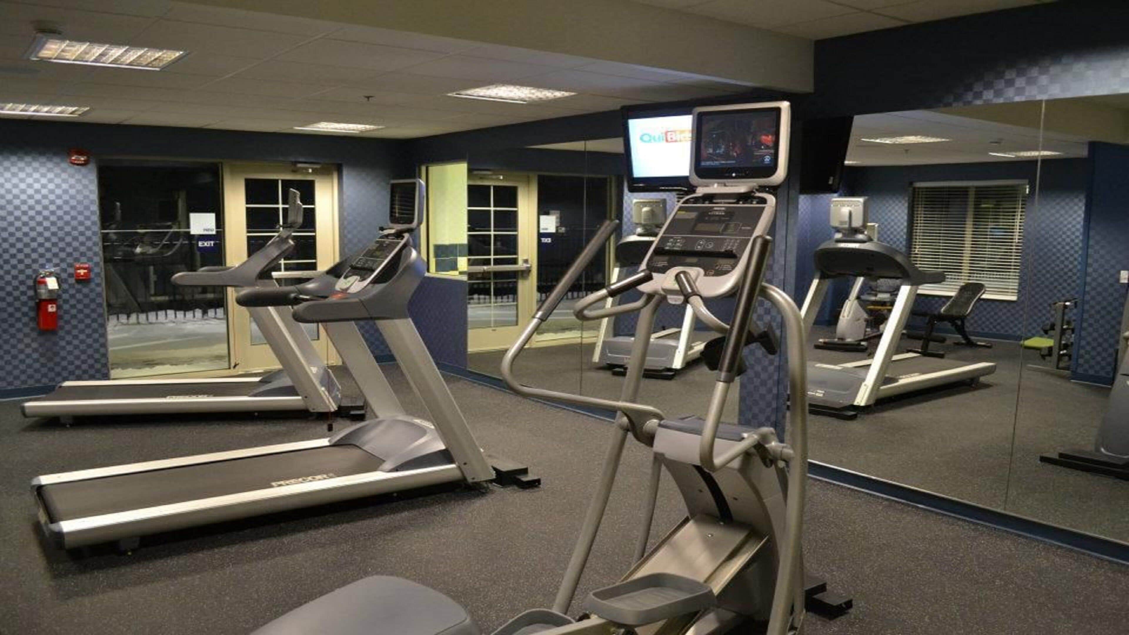 Un gimnasio con cintas de correr, elípticas y un espejo grande.