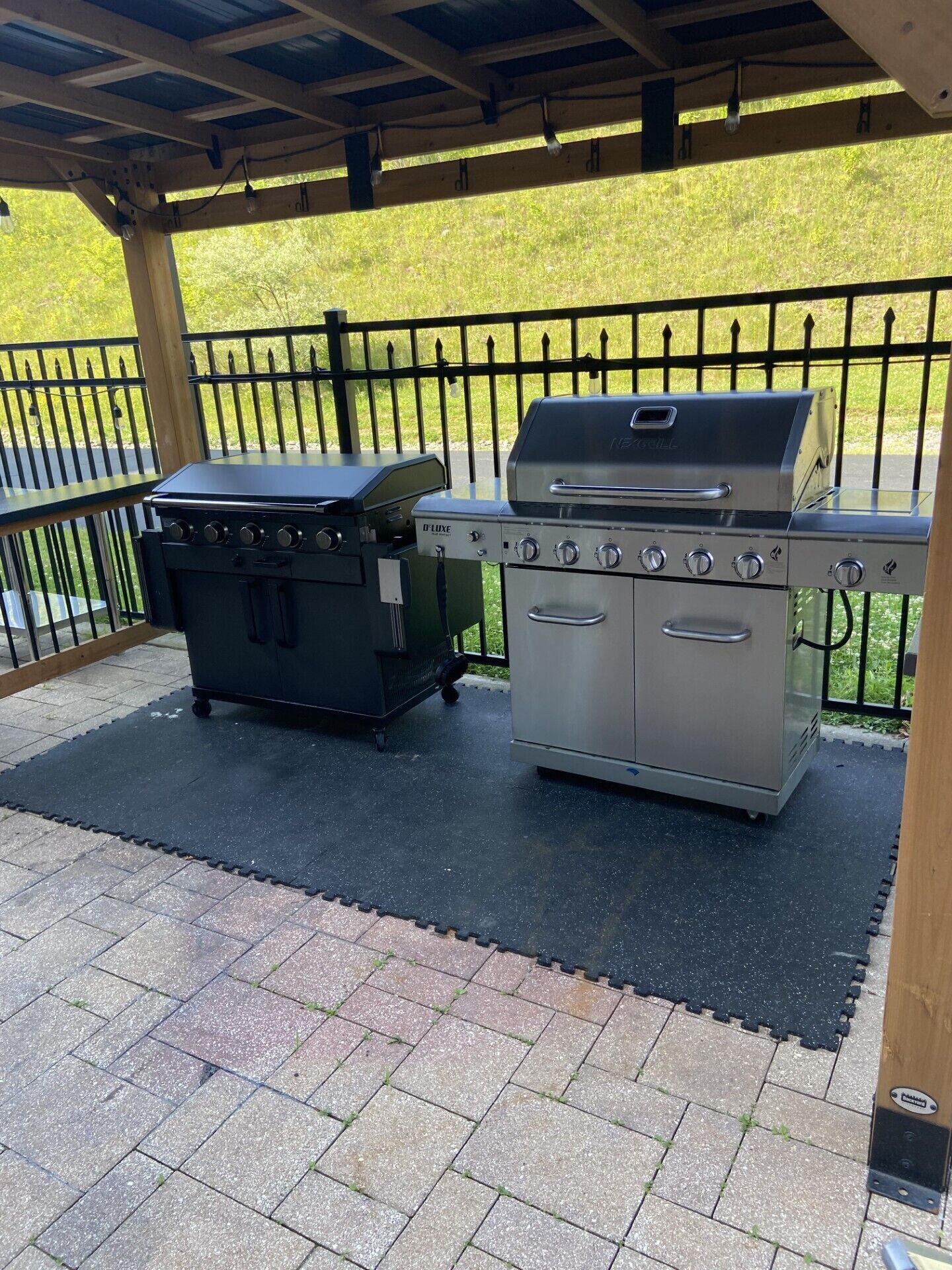 Zona de parrilla al aire libre con estufa a gas y parrilla de carbón bajo un porche cubierto.