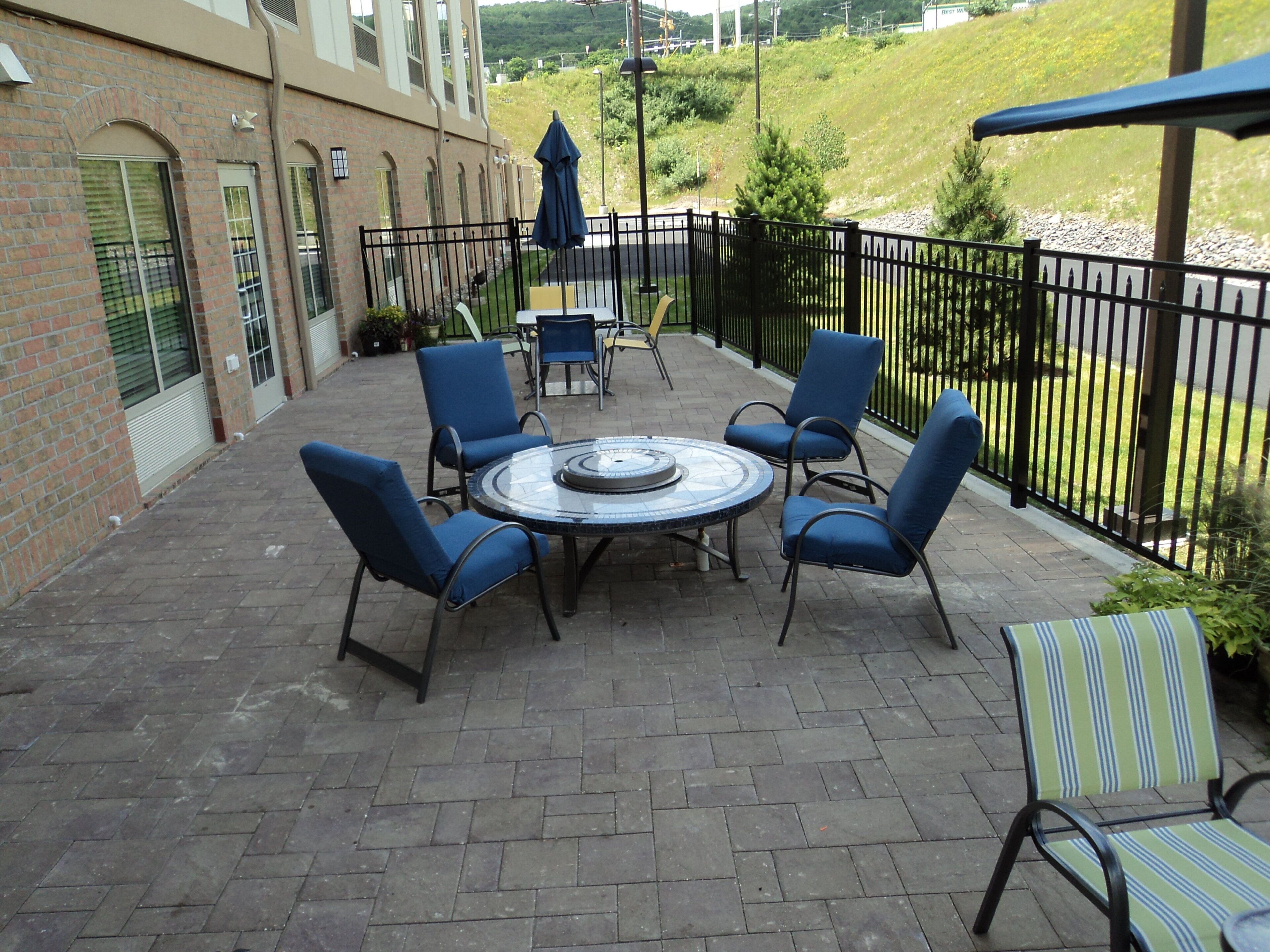 A patio with a round table and chairs, a brick wall, and a view of a green hillside.