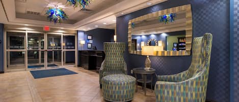 A lobby with a reception desk, two patterned armchairs, a mirror, and a blue wall.