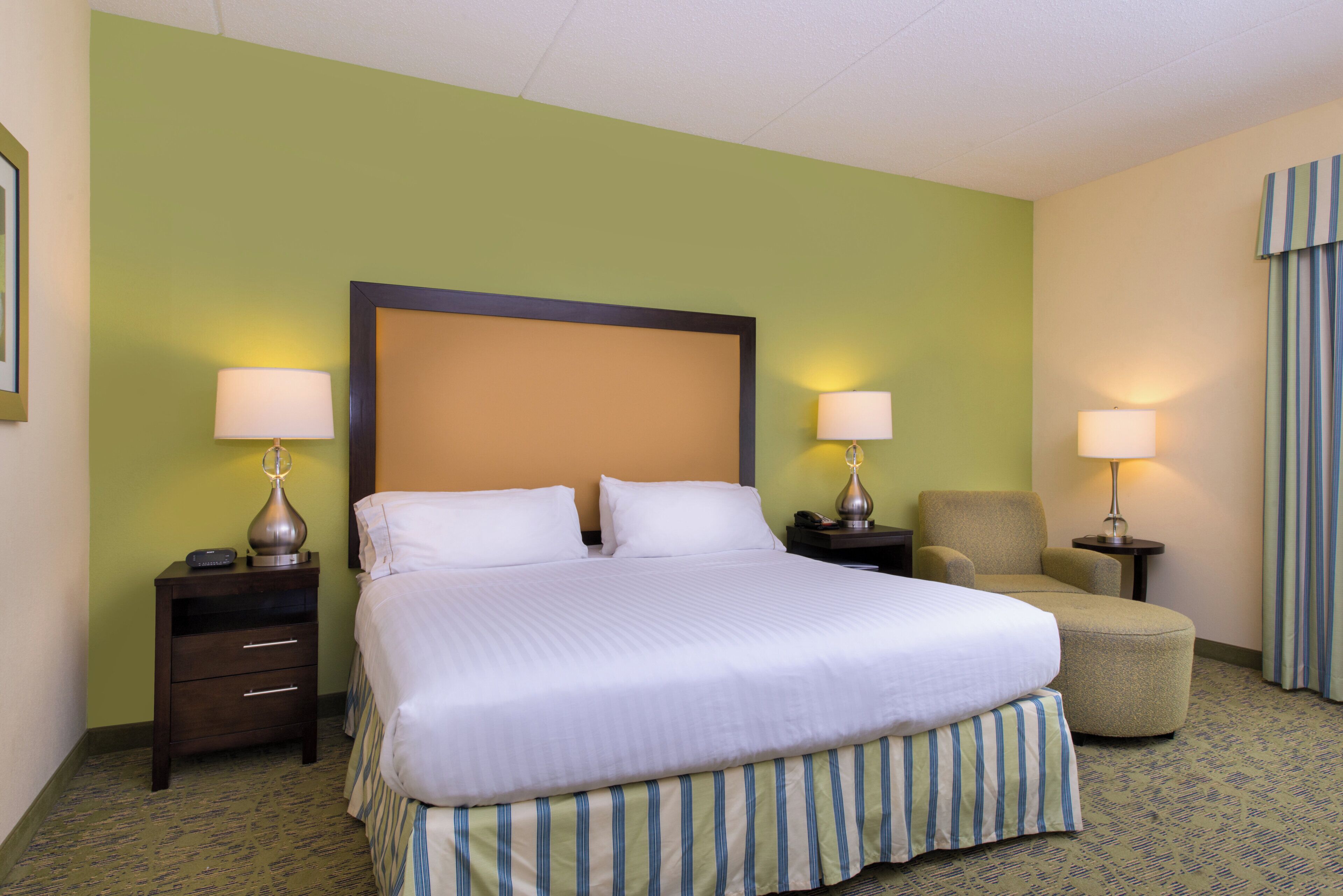 A hotel room with a large bed, two bedside tables with lamps, a chair, and a small table.