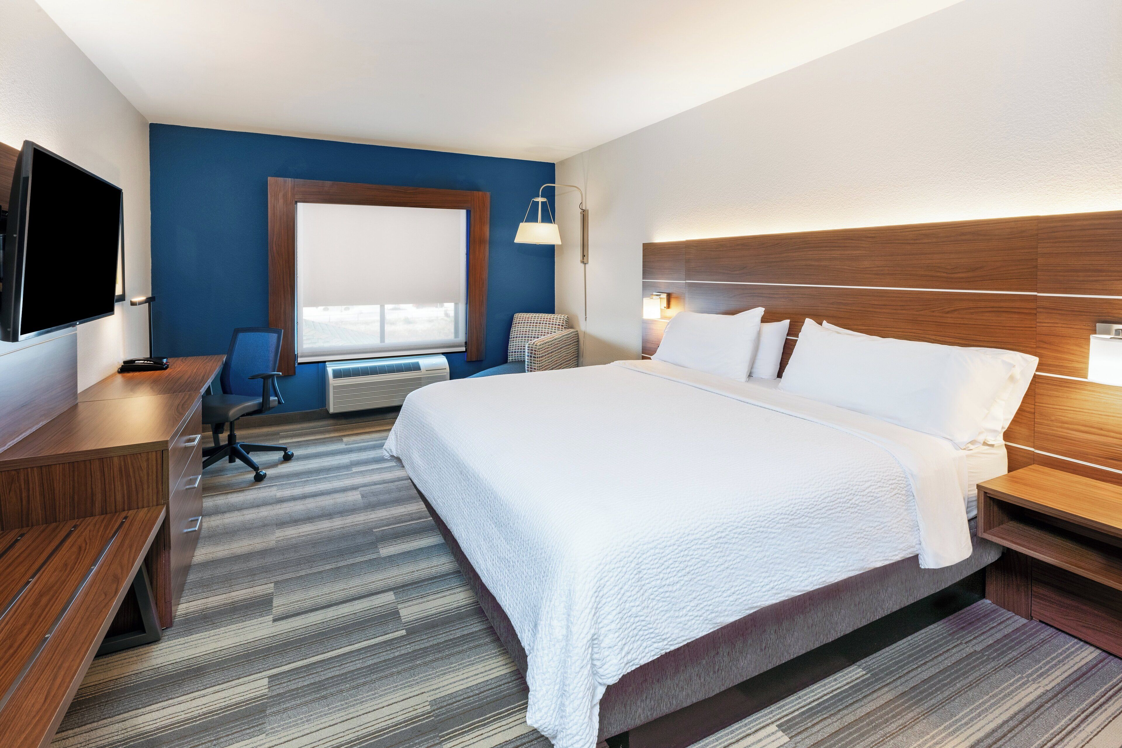 A hotel room with a large bed, a desk with a chair, a television, and a window with a view.