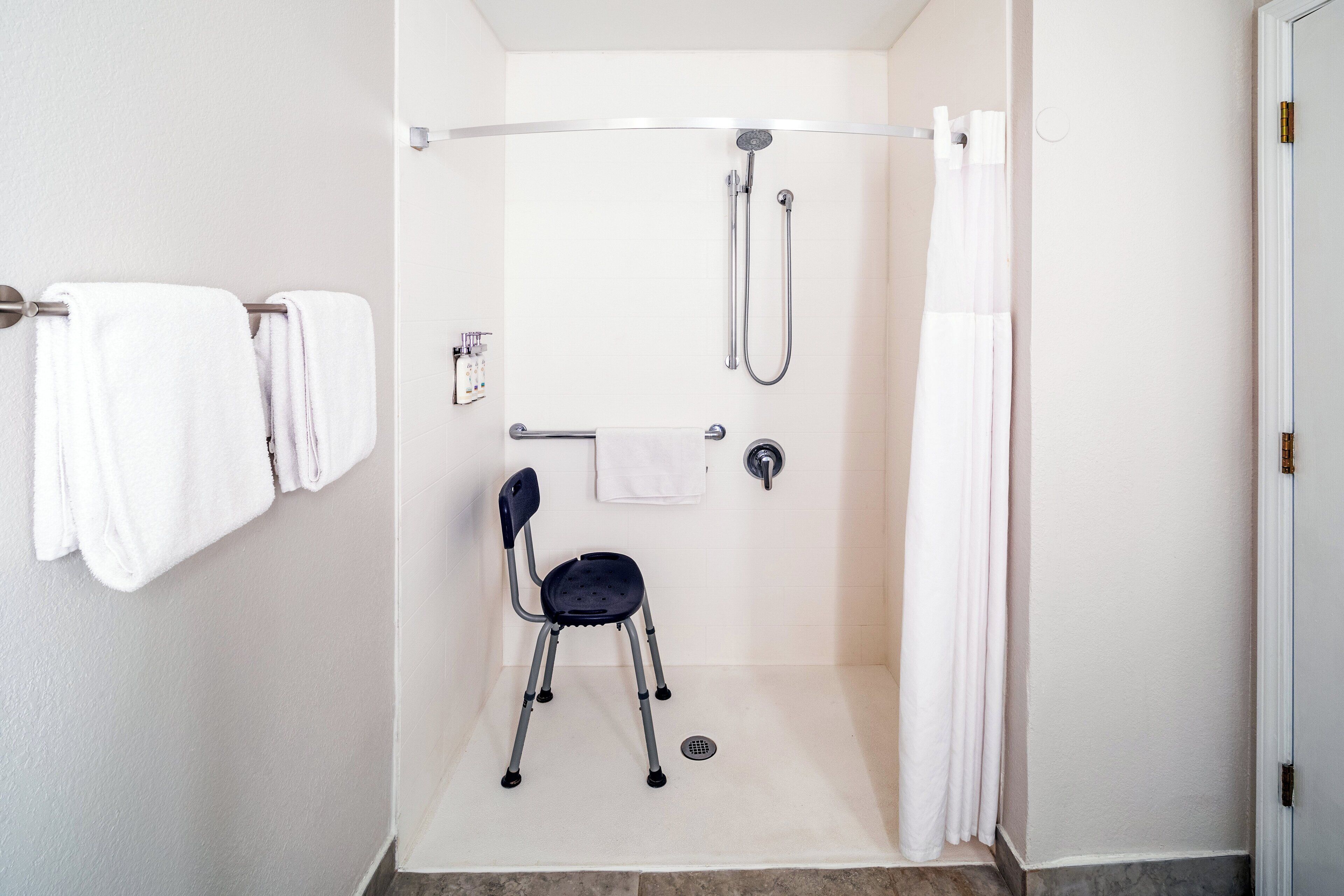 A shower area with a grab bar, a chair, and a towel rack.